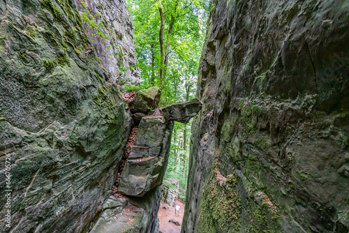 Rock stuck in a narrow rocky groove or walls of rock formations with different types of erosions, green leafy trees in background, sunny day in Teufelsschlucht nature reserve, Irrel, Germany photo