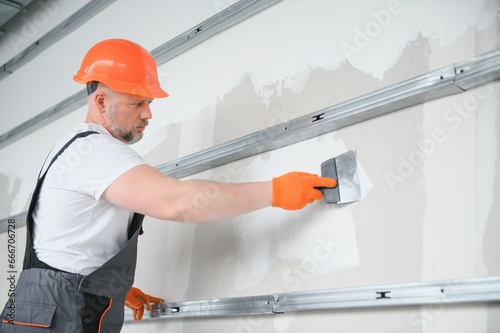 man drywall worker using trowel for plasterer putting stucco on plasterboard white wall. photo