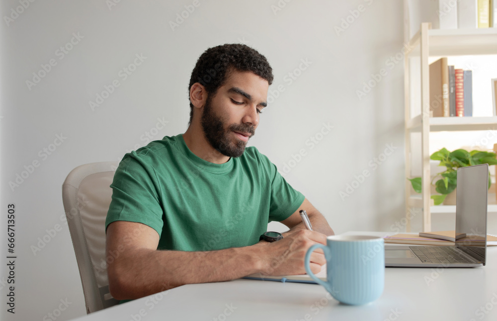 Man in green t-shirt daydreaming while jotting notes at home office Man in green t-shirt daydreaming while jotting notes at home office