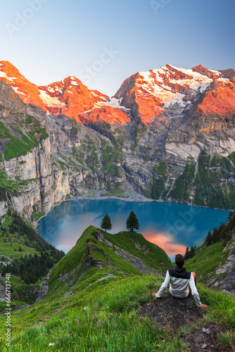 View of a hiker resting in front of the Oeschinensee lake surrounded by snowy peak at sunset, Oeschinensee, Kandersteg, Bern Canton, Switzerland photo