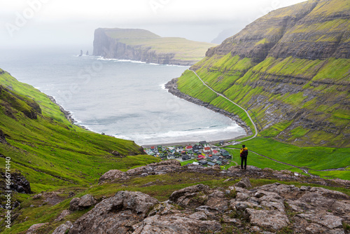 One man on top of a rock admiring the village of Tjornuvik in the misty weather, Sunda municipality, Streymoy island, Faroe islands, Denmark photo