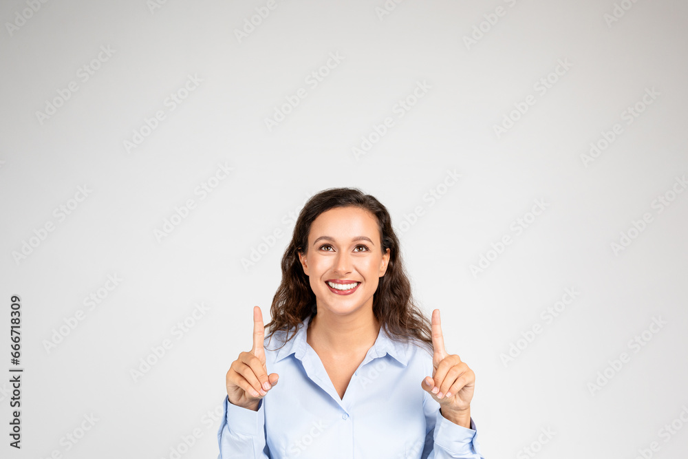 Smiling young european woman in formal wear pointing fingers up at copy space Smiling young european woman in formal wear pointing fingers up at copy space