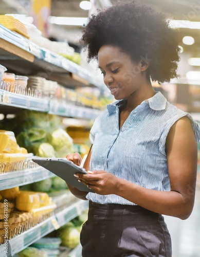 Trabalhadora profissional do sexo feminino usa tablet para pesquisar com lista de verificação em super mercado e distribuição, o valor dos preço dos produtos da sexta basica de alimentos. photo
