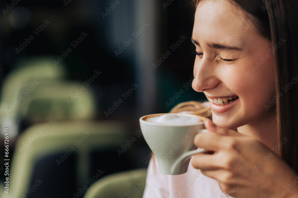 A young cheerful woman is laughing while drinking fresh coffee in a coffee shop. A young cheerful woman is laughing while drinking fresh coffee in a coffee shop.