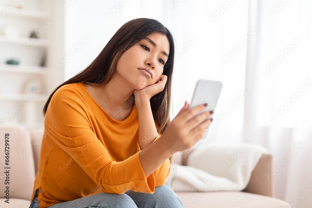 Bored asian young lady using mobile phone at home Bored asian young lady using mobile phone at home