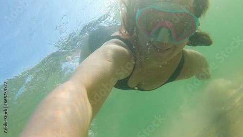 Girl in an underwater mask takes a selfie and blows a kiss underwater. Summer activity. Beautiful diver in sea water. Active recreation at sea. Water sports in the tropical sea. High-quality shooting
