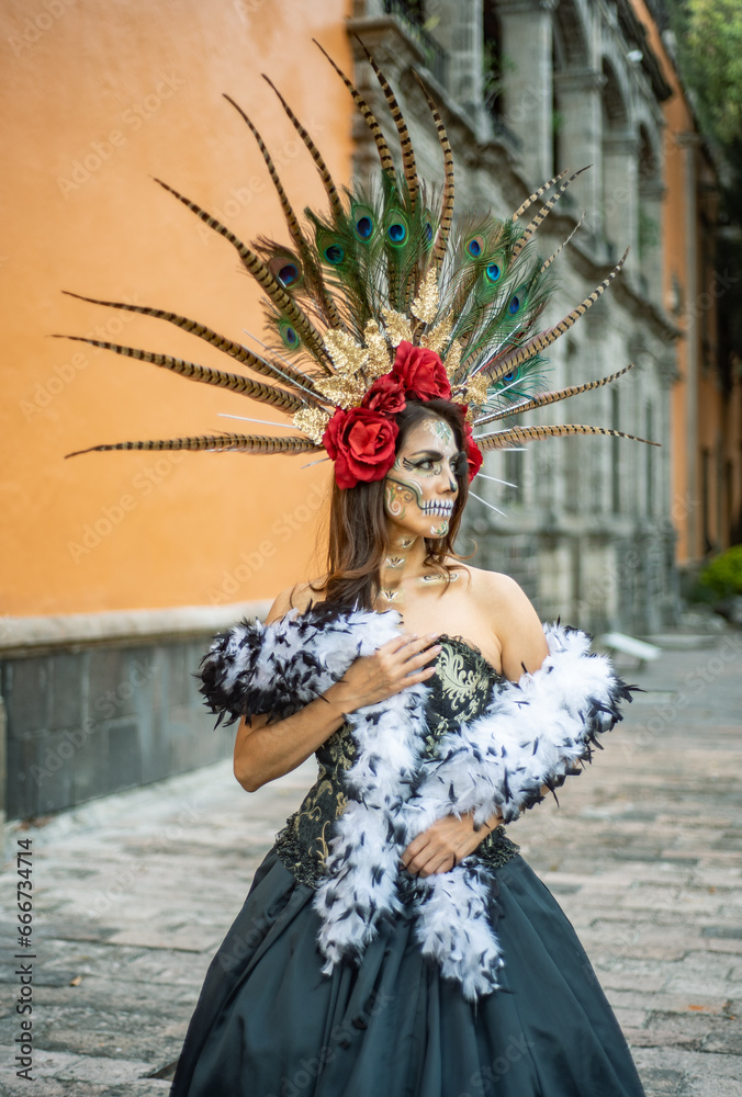 Catrina en Vestuario Tradicional Mexicano con tocado de plumas y flores rojas, grandes ojos y maquillaje de dientes y pestañas postizas