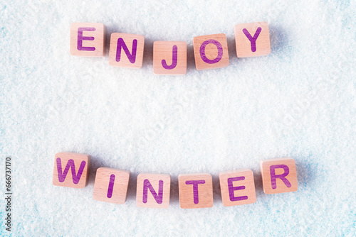 Wooden blocks and in snow with words Enjoy Winter. Concept of coming winter holidays