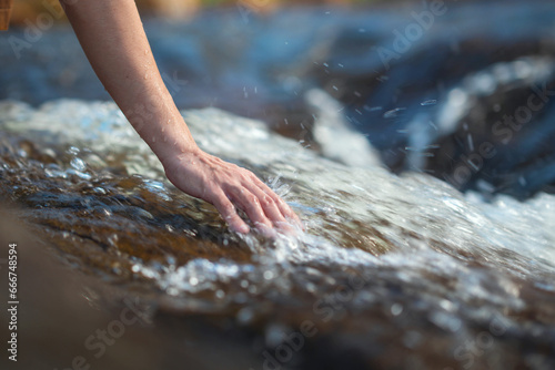 Close up hand of traveler woman touching water in the forest from waterfall, Tourist travel enjoying nature and life concept. Go everywhere.