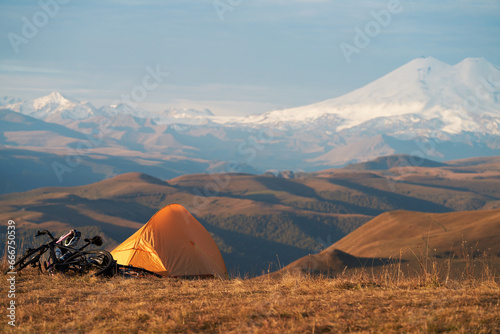 Morning in the mountains. Tourist tent against the background of snow-covered mountains. A sport bike is lying next to the tent. Copy space