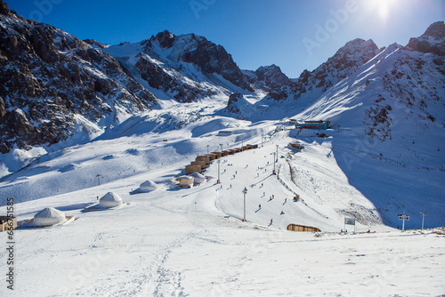 Shymbulak mountain resort's ski slopee with eco hotel, yurts, skiers and snowboarders. Skiers at slopes of ski resort Chimbulak.