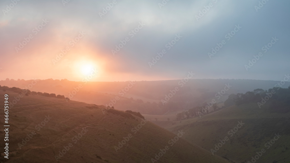 Stunning Summer sunrise from Devil's Dyke in South Downs National Park in English countryside with low lying clouds giving moody feeling