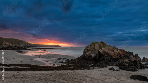 Beautiful sunrise landscape image of Kennack Sands in Cornwall UK wuth dramatic moody clouds and vibrant sunburst