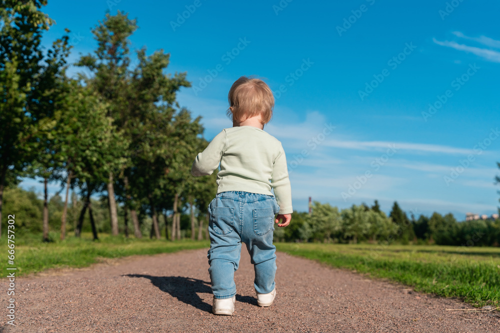 Rear view of little child baby 1 year in jeans in the park in summer, outdoor walking Rear view of little child baby 1 year in jeans in the park in summer, outdoor walking