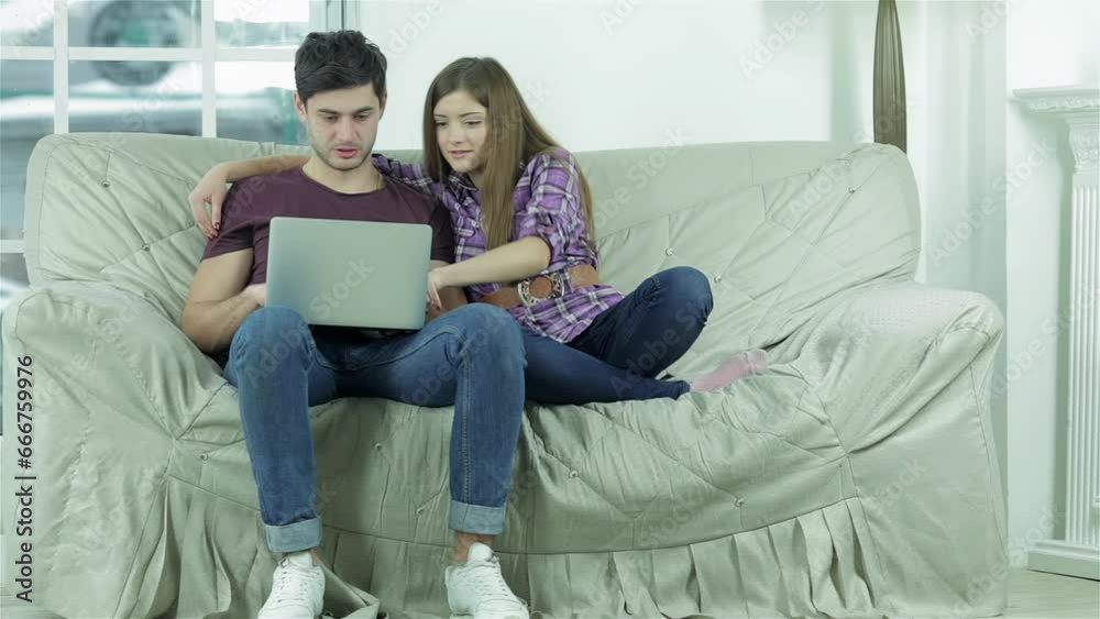 Girl hugging the shoulders of her boyfriend sitting on the sofa Girl hugging the shoulders of her boyfriend sitting on the sofa