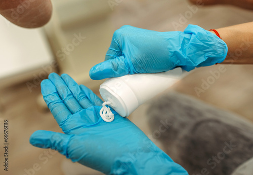 A podiatrist applies a massage cream from a tube to her hand.