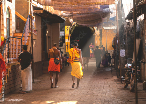 Morning in Gokarna, people walking along a street illuminated by sunlight. Karnataka state, India