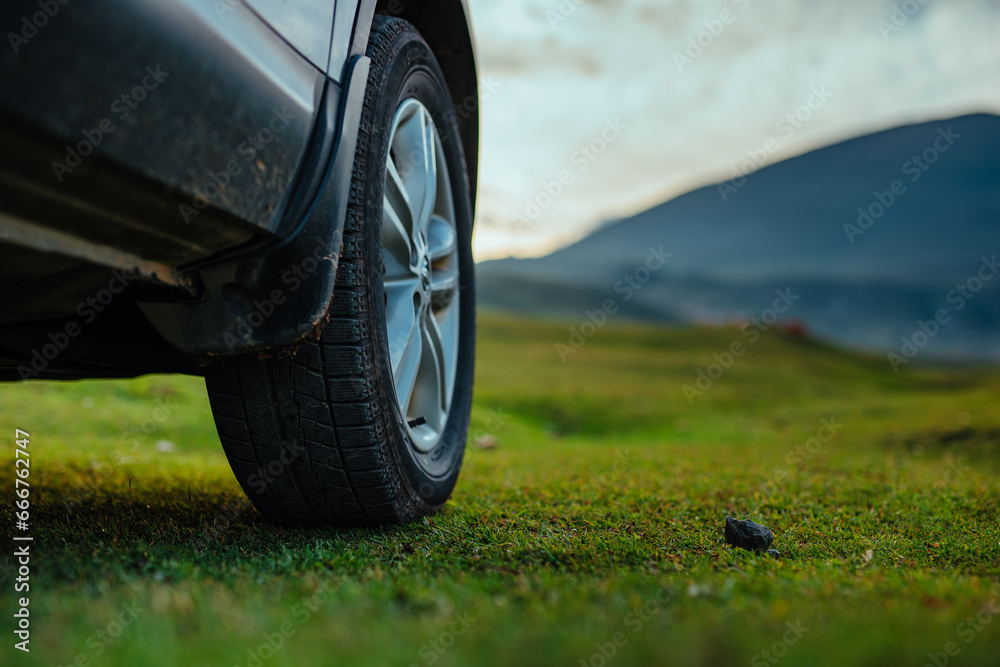 Car wheel on green grass in mountain valley close-up view