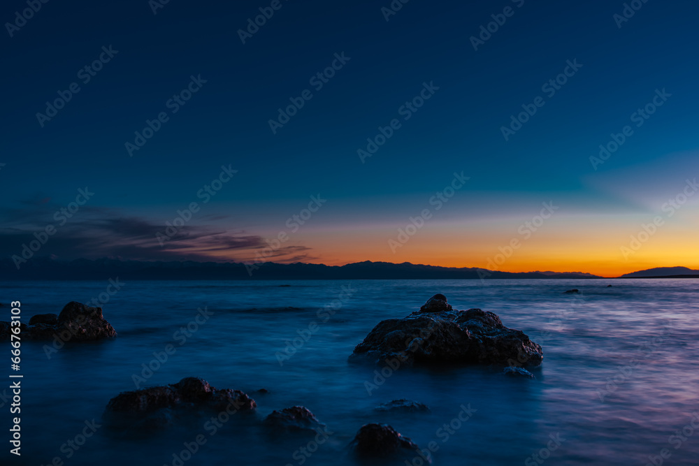 Fototapeta premium Lake landscape with big stones at dark sunset, long exposure blurred motion