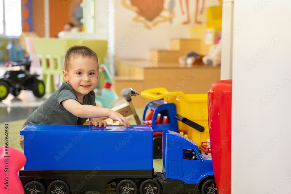 A happy smiling toddler boy plays with a big blue car in a children's entertainment center. Children's room. Childhood and spending time with toys A happy smiling toddler boy plays with a big blue car in a children's entertainment center. Children's room. Childhood and spending time with toys