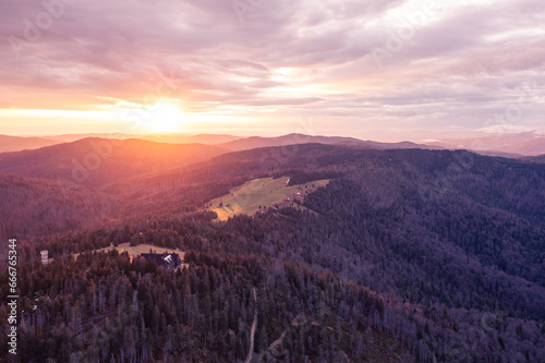 Panorama of beautiful sunrise over the forest hills. Green meadow in the center of the frame. Visible roof of a mountain hut. Drone photo.  © michnik101