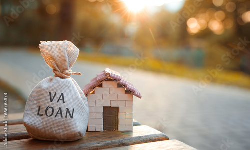 Va loan concept - government-backed mortgage option available to Veterans, service members and surviving spouses. Money bag and miniature house in the park in the sunset light. Real estate and finance photo