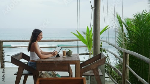 Wallpaper Mural Young illustrator drawing on tablet at cafe with ocean view, palm trees. Pretty focused woman works remotely at authentic bar near tropical coast. Freelancer editing illustration at the seaside. Torontodigital.ca