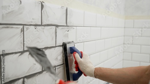 Working grouting of tiles, applying grout to the seam of tiles for home renovation in the kitchen. Applying grout to ceramic mosaic tiles. Working hands work with ceramic tiles. photo