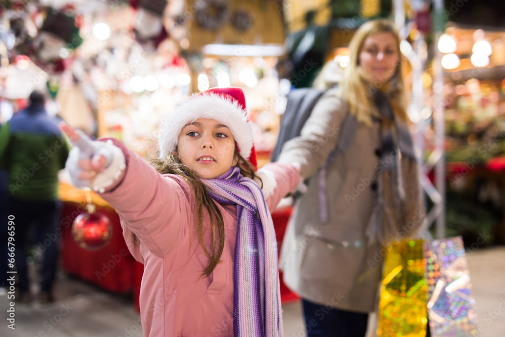 Young mother with her daughter shopping on outside Christmas market pointing to something