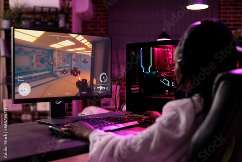 Woman in cozy apartment playing captivating video game on gaming PC at computer desk late at night. Sleepy gamer girl battling villains in multiplayer science fiction shooter