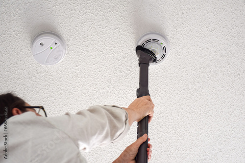 Woman vacuuming smoke and carbon monoxide detectors on a ceiling of a domestic room photo