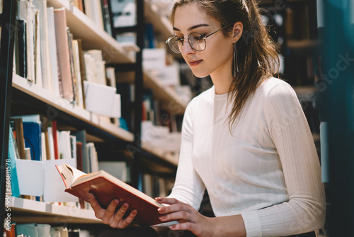 Attractive female hipster in casual wear learning with book at library