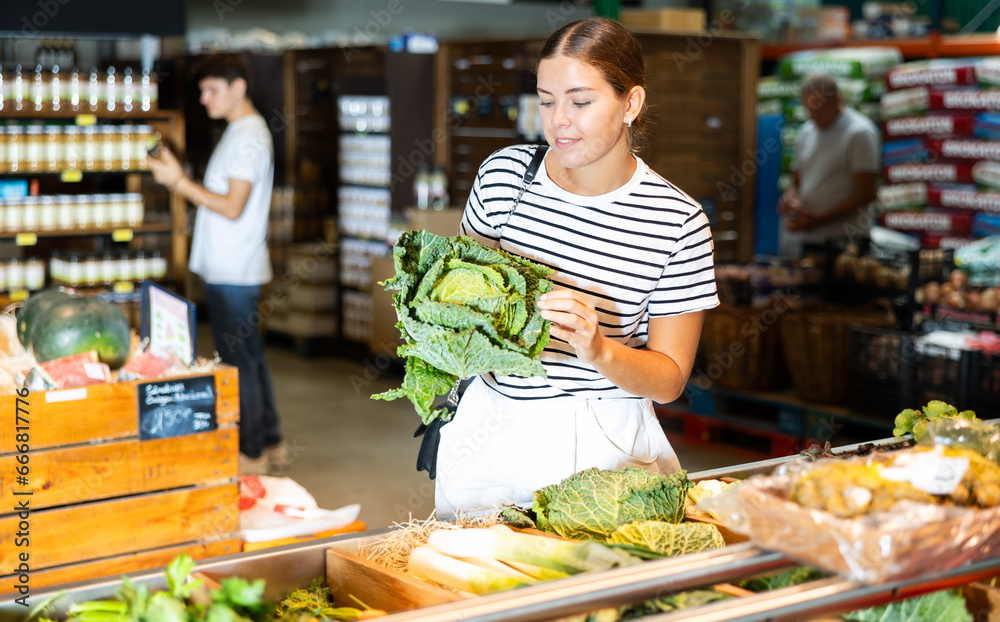 Young woman shopper choosing cabbage in grocery store