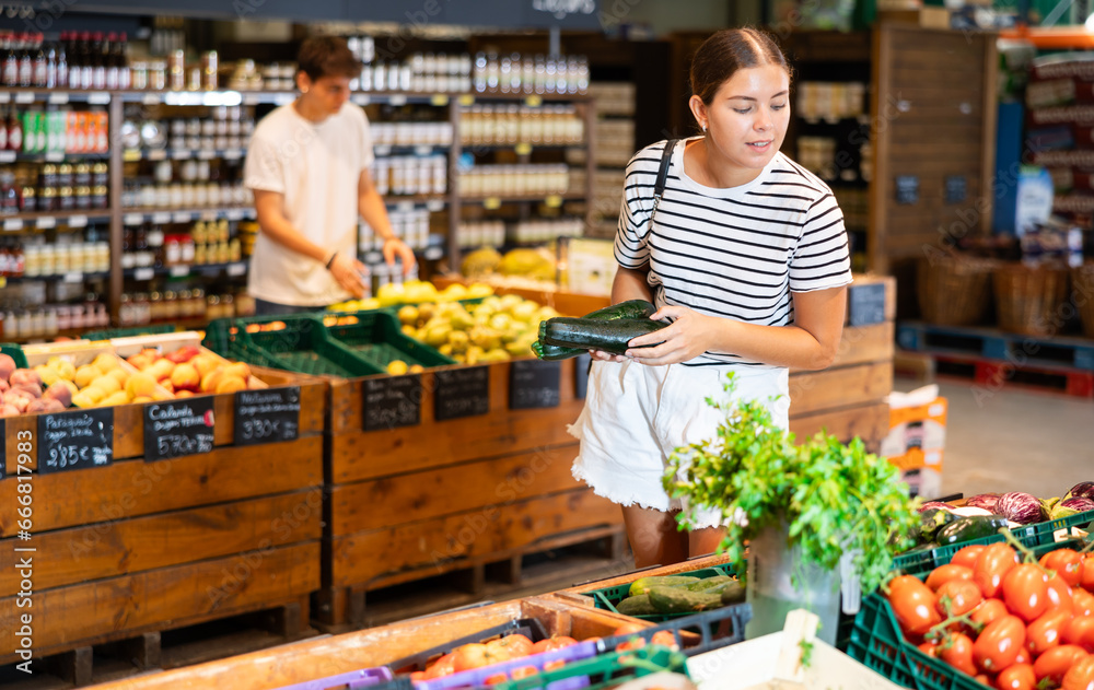 Young woman shopper choosing zucchini in grocery store