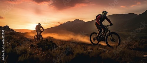 Two mountainbikers riding down a mountain at sunset.