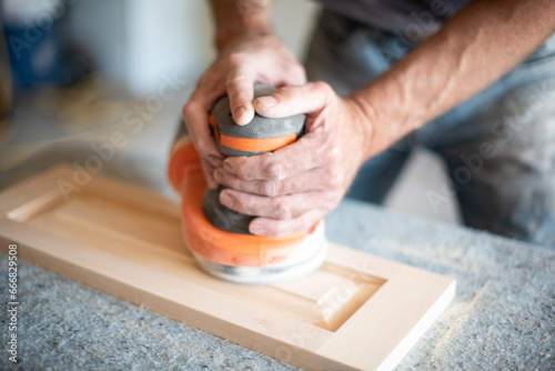 Carpenter's hands using power sander on woodwork