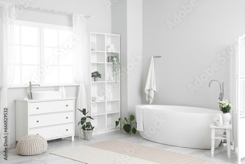 Interior of light bathroom with sink  bathtub  shelving unit and houseplants