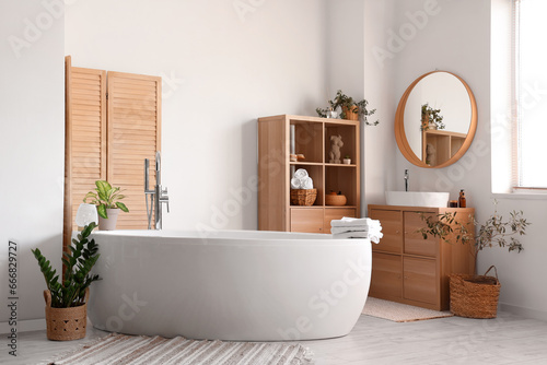 Interior of light bathroom with white sink  shelving unit and bathtub