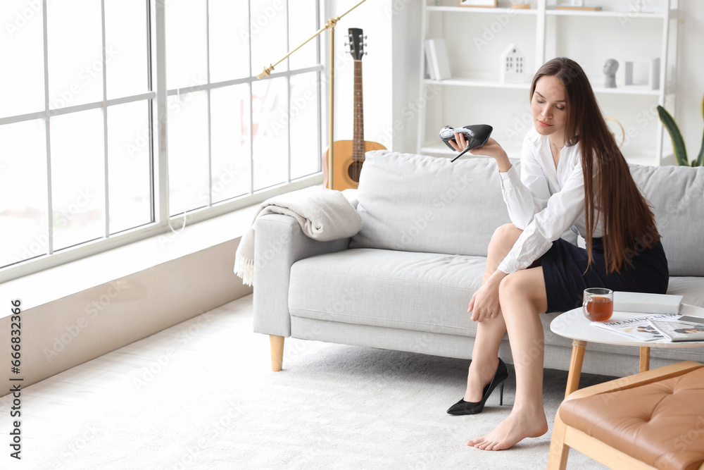 Young businesswoman taking her shoes off at home after long working day Young businesswoman taking her shoes off at home after long working day