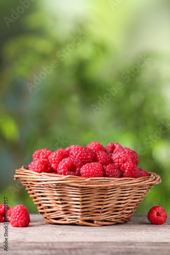 Wicker basket with tasty ripe raspberries on wooden table against blurred green background, space for text