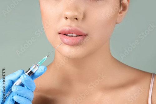 Young woman receiving lip injection on green background  closeup
