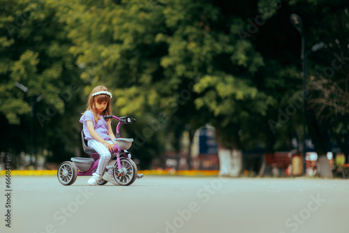 Unhappy Little Girl Sitting on a Tricycle Alone in a Park. Stressed child feeling upset trying to ride a bike 