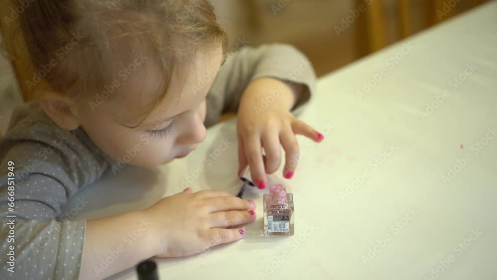 A little girl paints her nails with pink polish. The girl paints her nails like an adult. A little girl paints her nails with pink polish. The girl paints her nails like an adult.