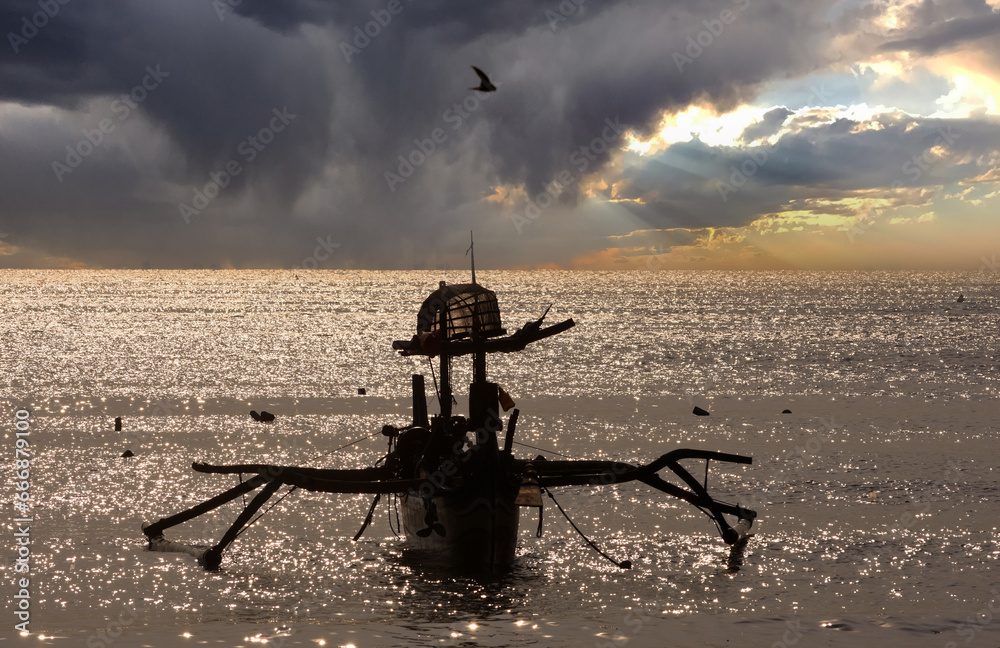 Silhouette of a fishing boat resting on the beach, against a dramatic sky background with birds flying in the clouds
