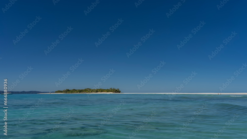 Idyllic seascape. The bottom can be seen through the clear turquoise water of the ocean. In the distance there is an island with tropical vegetation on a sandy beach. The boat is moored at the shore.