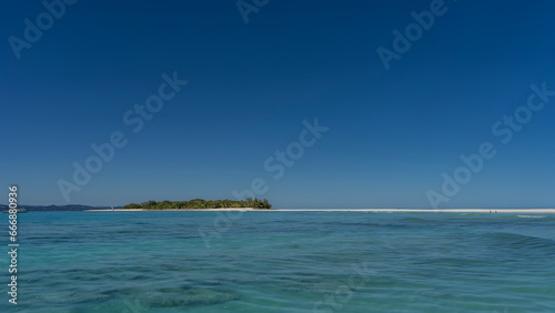 Idyllic seascape. The bottom can be seen through the clear turquoise water of the ocean. In the distance there is an island with tropical vegetation on a sandy beach. The boat is moored at the shore.