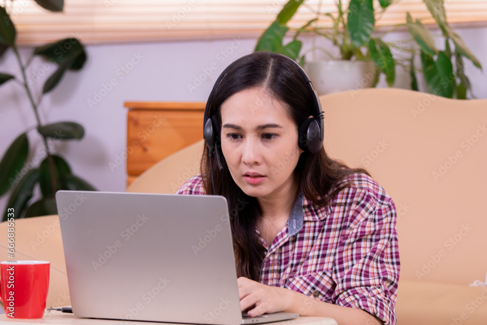 Asian woman sitting on floor remote working at home online small business using headphone with microphone and laptop conference with customer, modern freelancer female design work on computer Asian woman sitting on floor remote working at home online small business using headphone with microphone and laptop conference with customer, modern freelancer female design work on computer