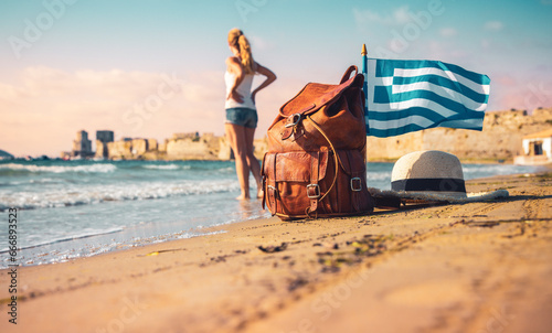 Travel destination in Greece-Traveler woman with bag, hat and Greek flag on the beach- Road trip, Adventure, summer vacation concept photo