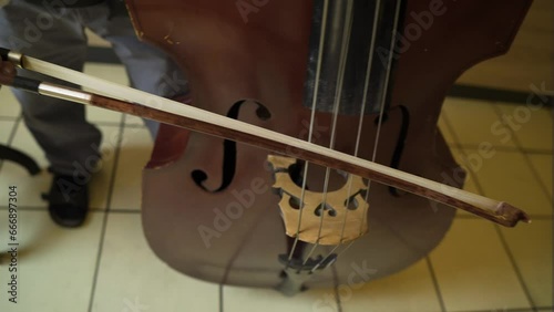close up of a contrabass cello bass and a man wearing black sandals holding a stick to make the sound baroque era classical royal sounds played inside kingdom palace for important people man standing photo