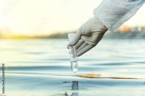 Fence, check the water sample for infections. Gloved hand with a flask and a test tube on a background of lake, river, sea. Pollution of ecology, environment photo
